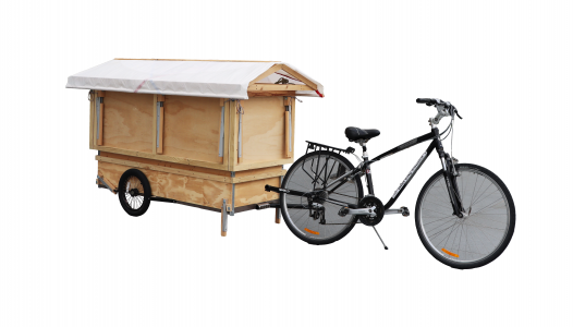 A bicycle connected to a wooden trailer that looks like a small house.